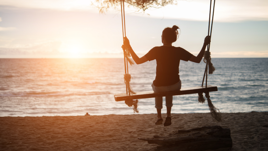 girl on swing facing out to the ocean watching sunset
