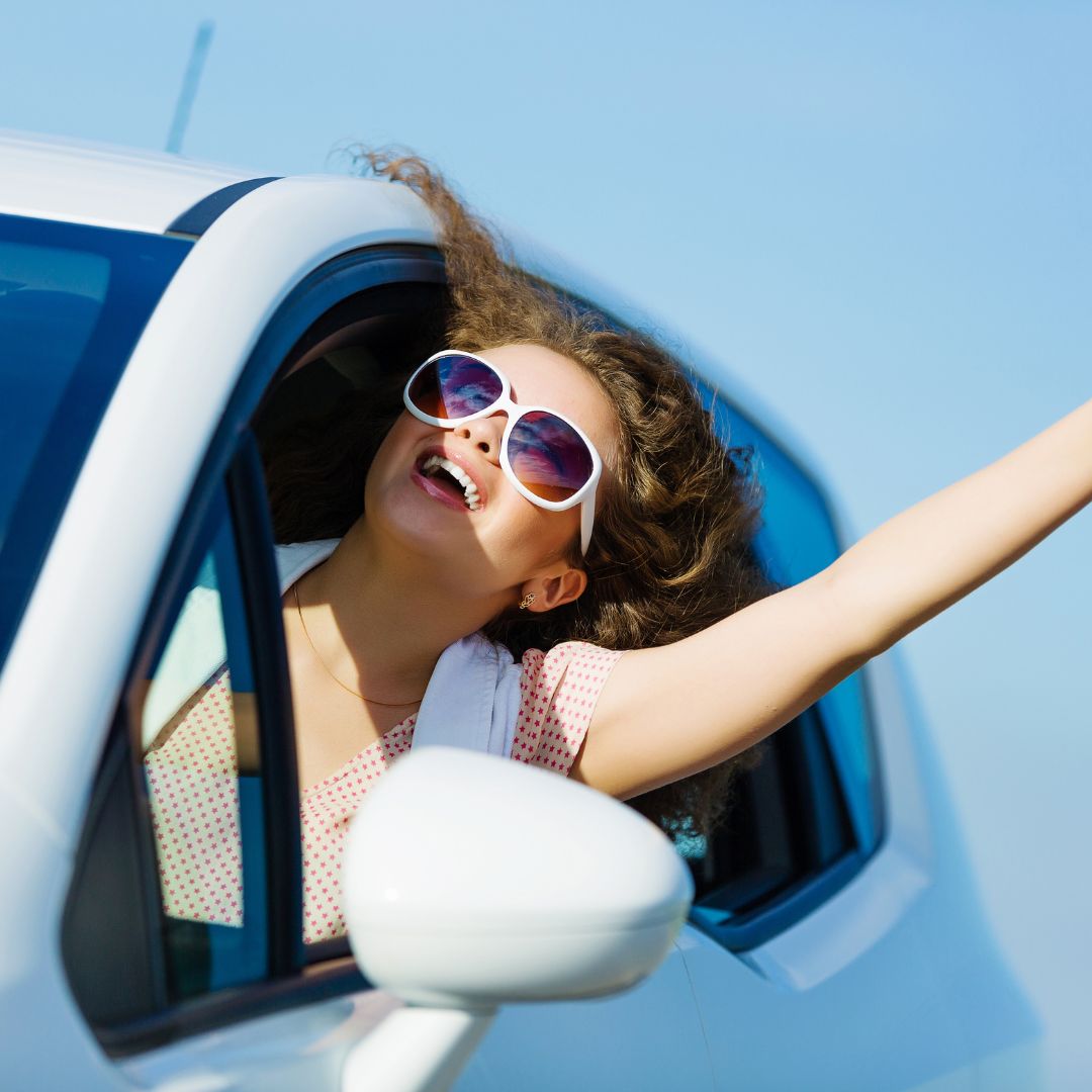 woman smiling hanging out window of car with sunglasses